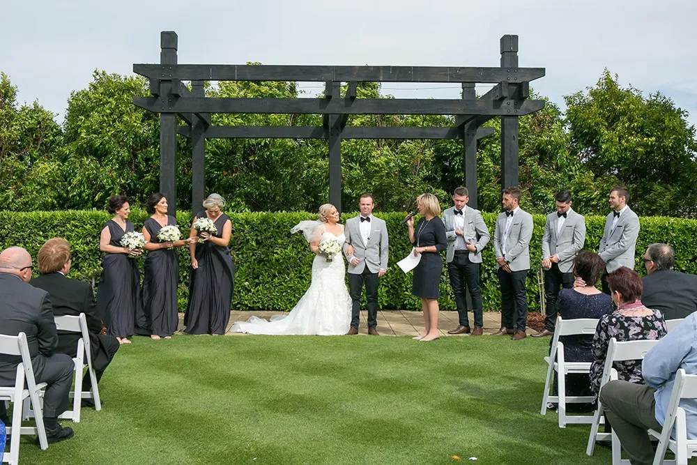Bridal party under a timber pergola during a garden wedding ceremony
