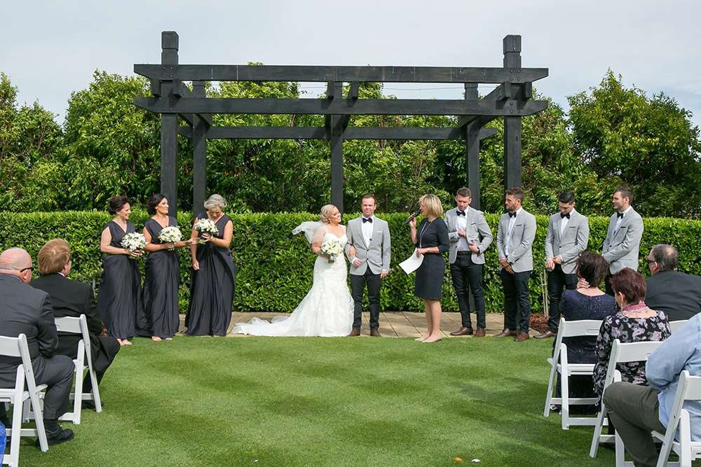 Bridal party under a timber pergola during a garden wedding ceremony
